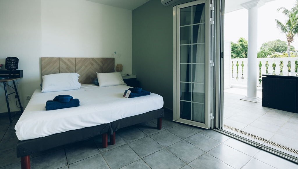 Chambre supérieure avec des portes-fenêtres ouvertes accédant à la terrasse, laissant entrer la lumière.