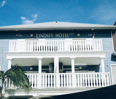Vue de la façade blanche et bleue à étages du Lindsey Hôtel avec ses balcons en bois.