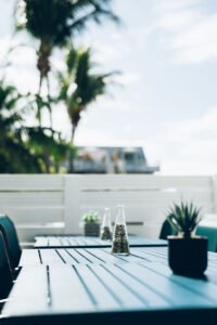 Terrasse ensoleillée bordant une piscine aux eaux turquoise, équipée de tables de jardin et de fauteuils en résine tressée pour les repas en plein air