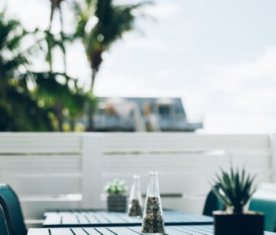 Terrasse ensoleillée bordant une piscine aux eaux turquoise, équipée de tables de jardin et de fauteuils en résine tressée pour les repas en plein air