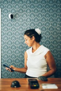 Une personne souriante regarde son smartphone devant un mur bleu à motifs géométriques blancs.