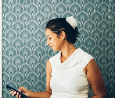 Une personne souriante regarde son smartphone devant un mur bleu à motifs géométriques blancs.