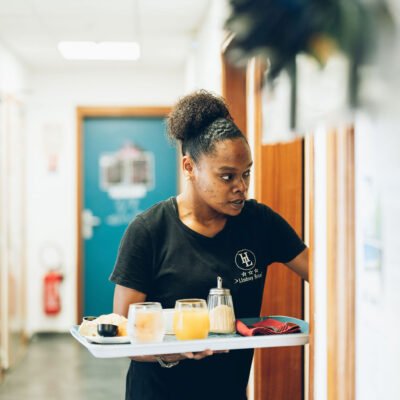 Une employée porte un plateau de petit-déjeuner avec des jus de fruits et des collations dans un couloir.