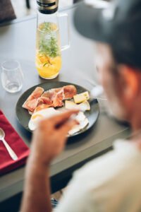Un homme attablé s'apprête à manger son petit-déjeuner face à une carafe de jus frais