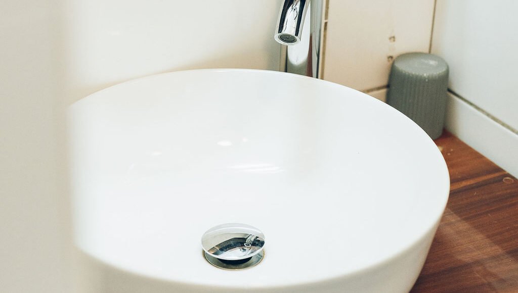 ue rapprochée d'une vasque blanche moderne posée sur un plan de toilette en bois, accompagnée d'un robinet chromé.