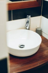 ue rapprochée d'une vasque blanche moderne posée sur un plan de toilette en bois, accompagnée d'un robinet chromé.