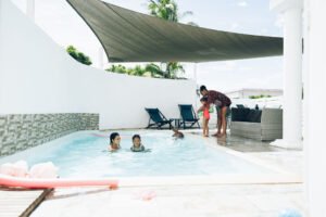 Plusieurs personnes profitent de la piscine et de l'espace détente sous une voile de protection solaire.