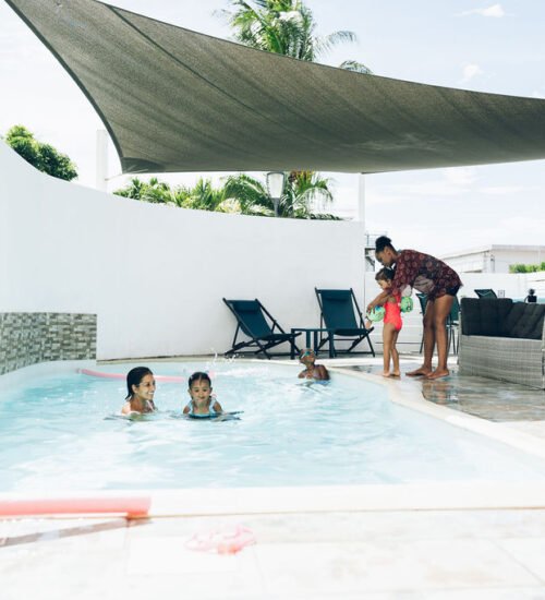 Plusieurs personnes profitent de la piscine et de l'espace détente sous une voile de protection solaire.